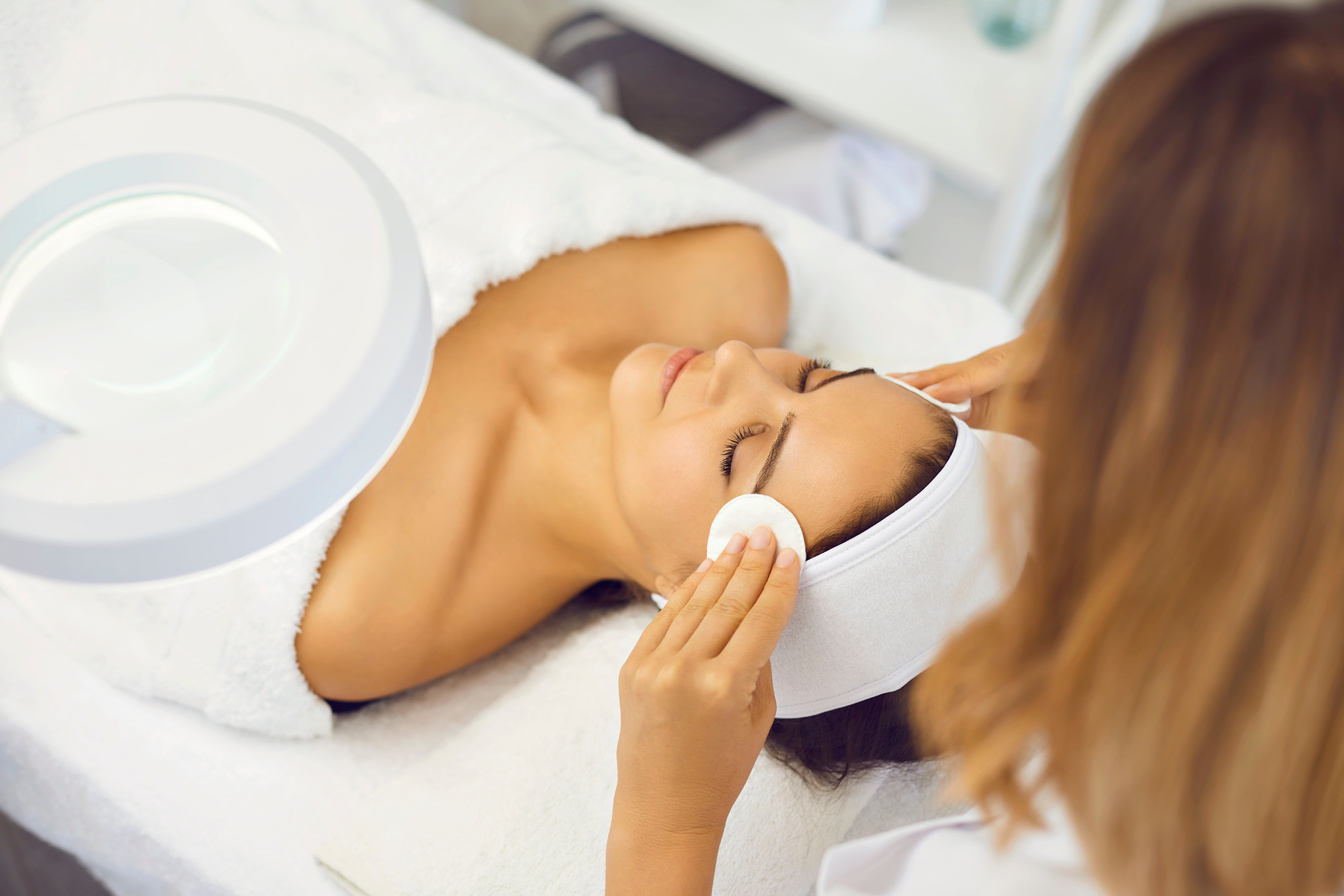 Cosmetologist Cleaning Woman Facial Skin with Cotton Pads before Massage in Beauty Salon